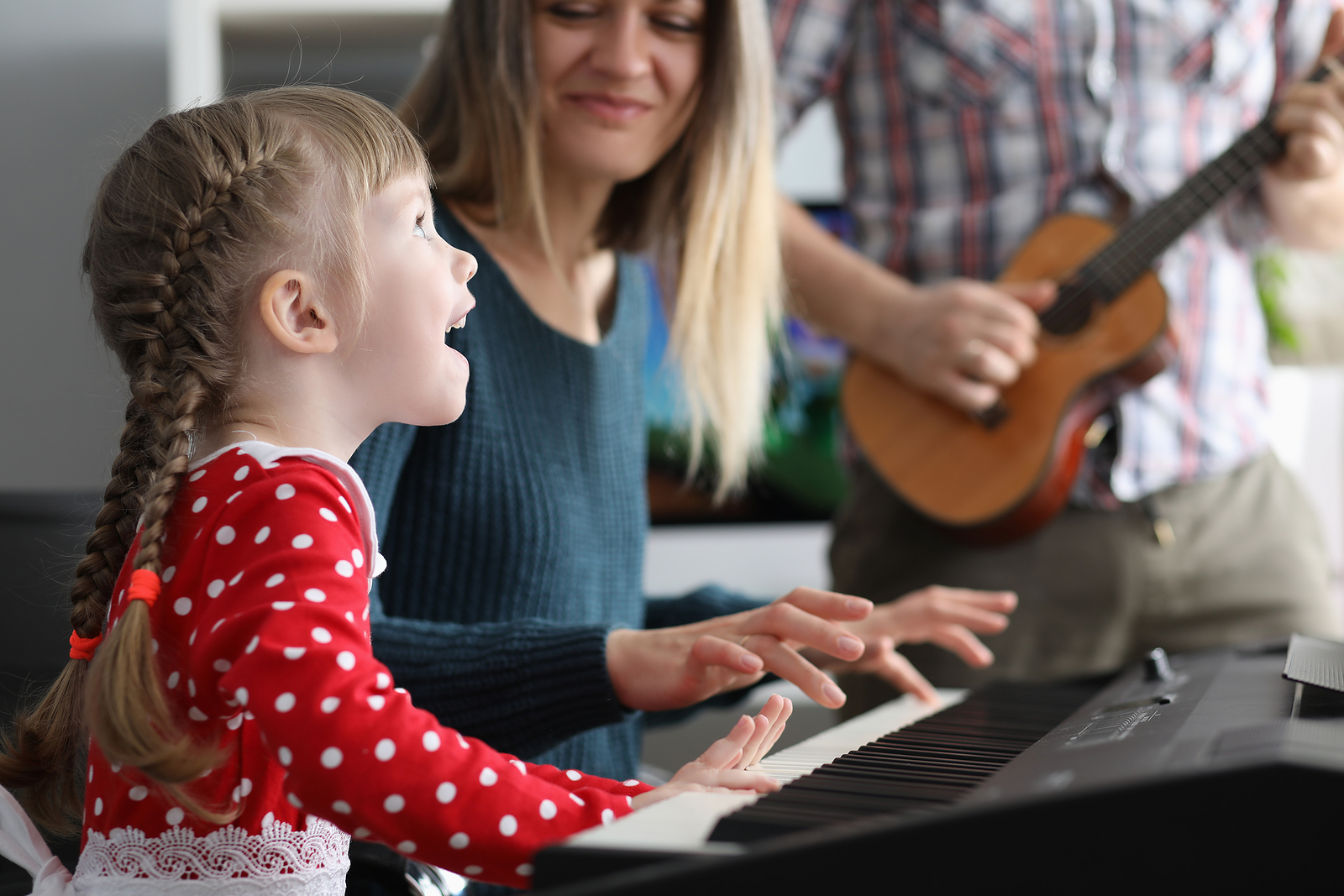 Little beautiful girl sings song is played on piano together with her parents portrait. Classes at music school for children concept.