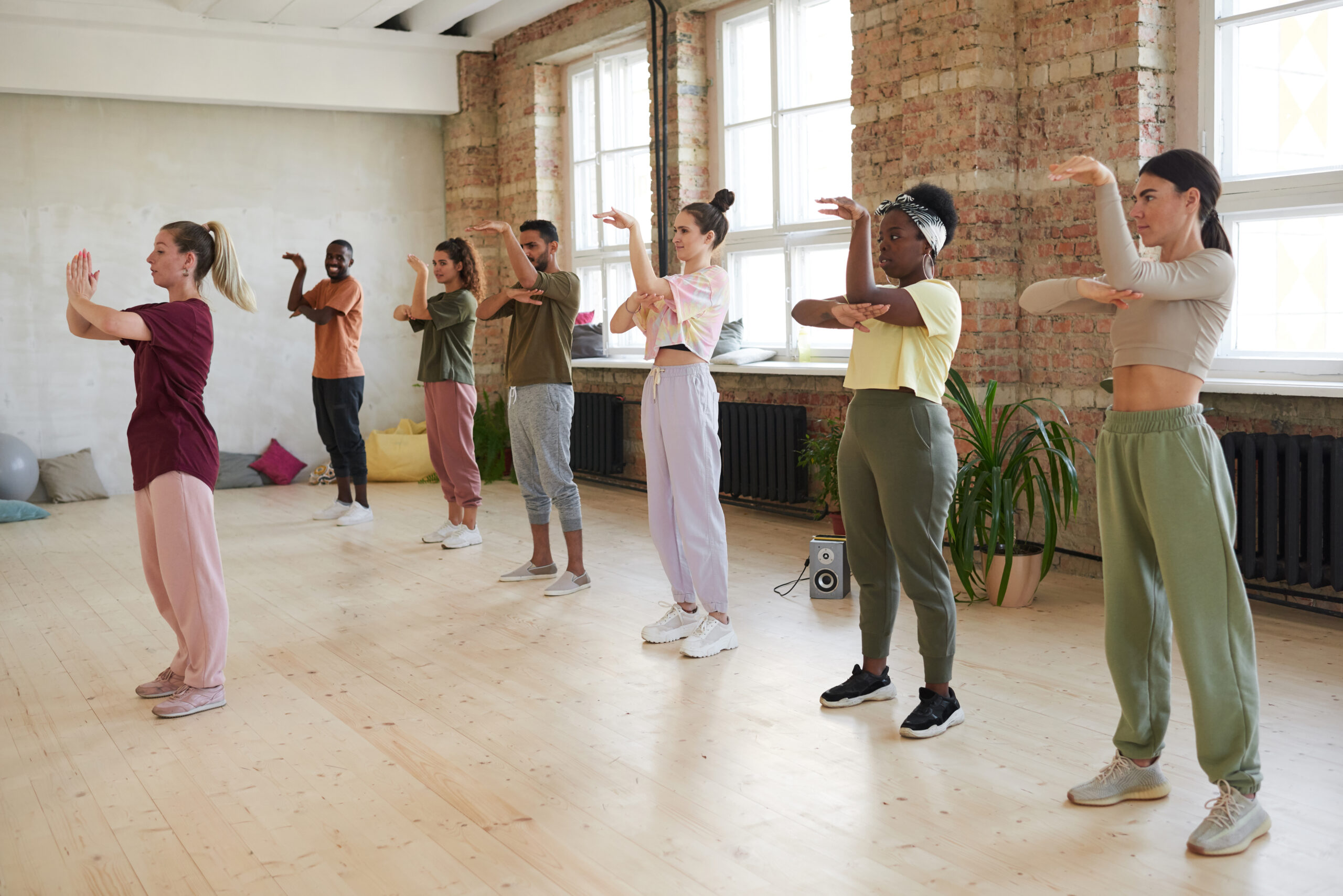 Group of people standing and repeating the movements of the instructor in dance exercise class
