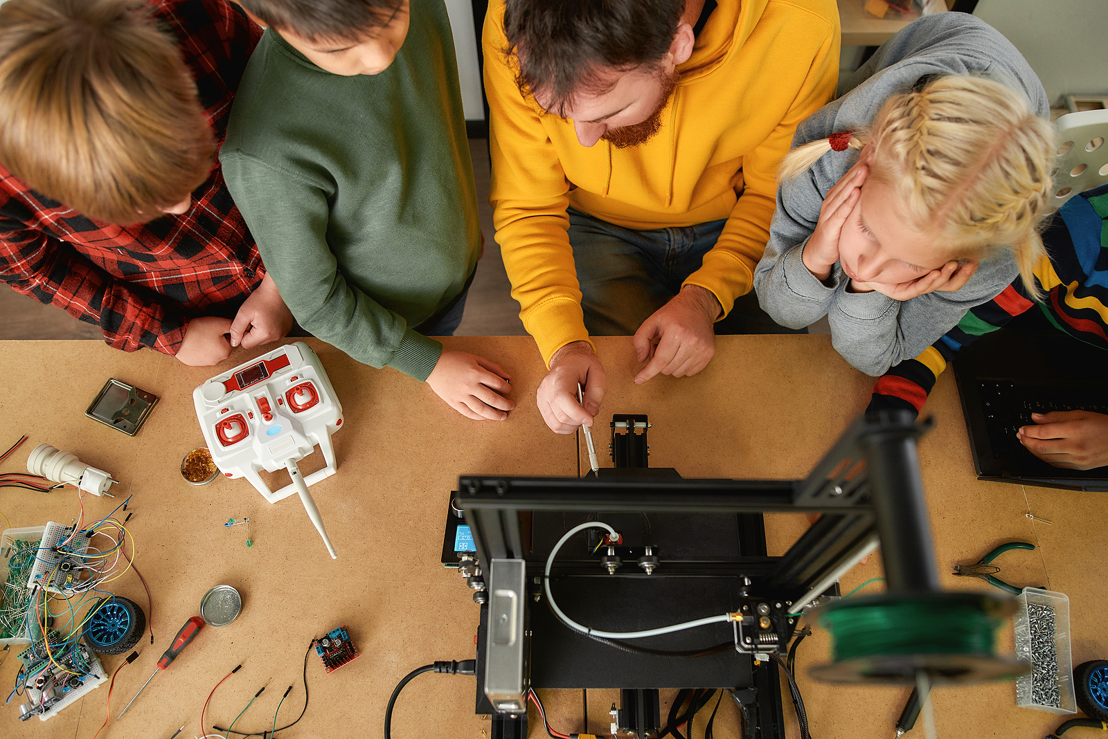 Young male teacher explaining to a group of curious kids working principle of 3d printer at robotics school lesson. Science and education. Top view